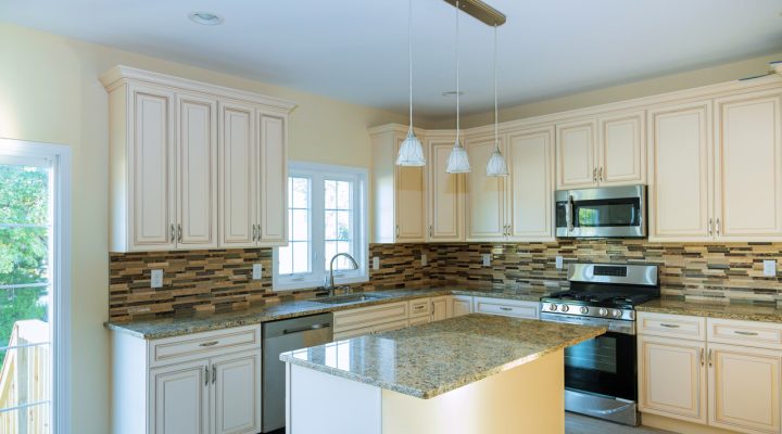 an L-shaped kitchen with a granite counter top, hanging cabinets and silver and black appliances